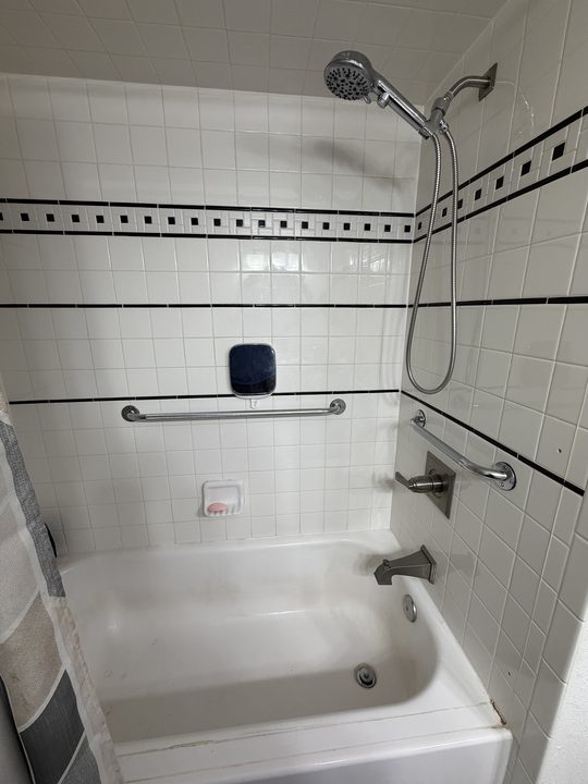 After: tiled tub and shower with a grab bar on the back wall and one on the side wall
